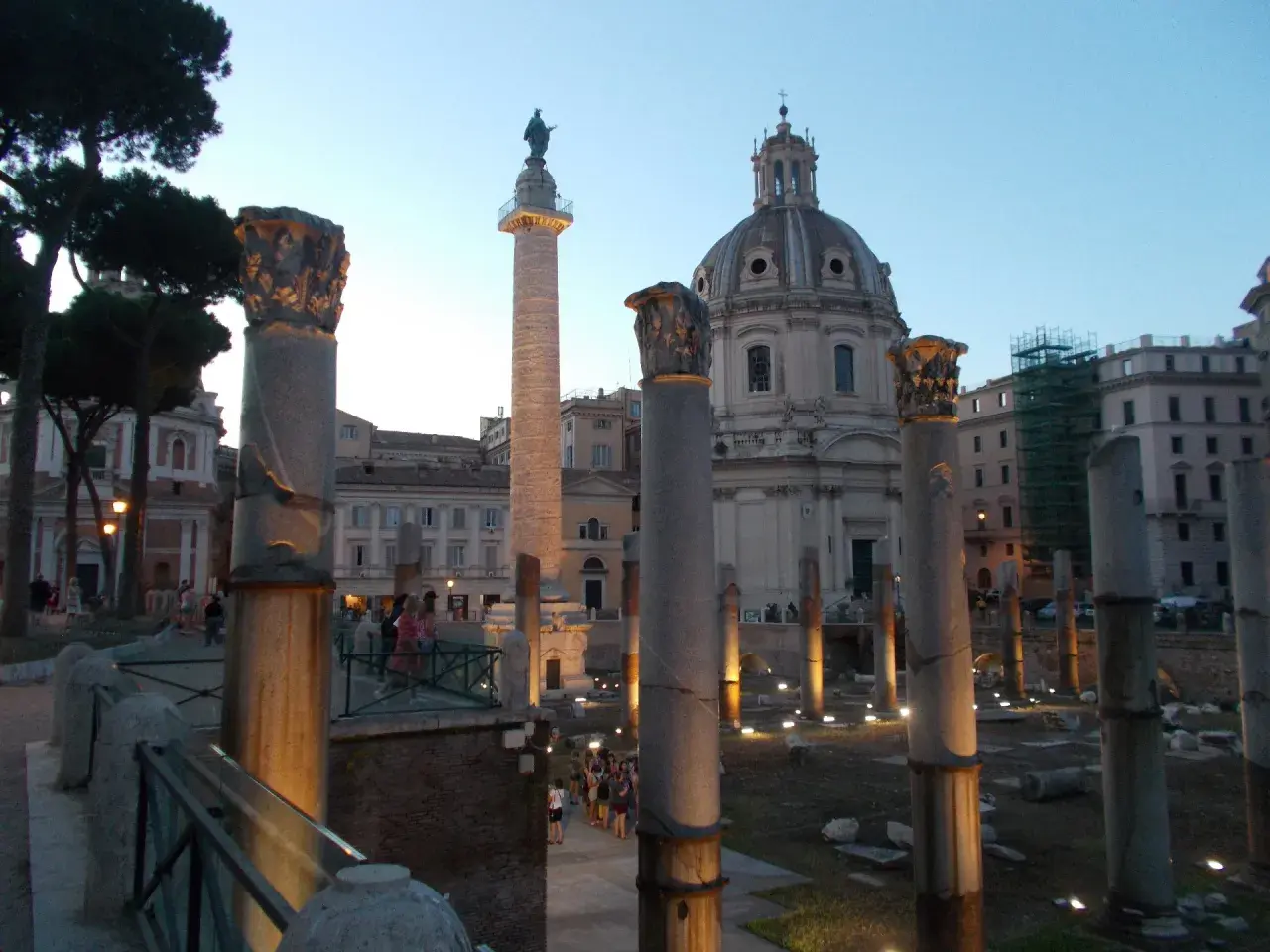Antiche colonne onorarie illuminate di sera, con una cupola sullo sfondo.