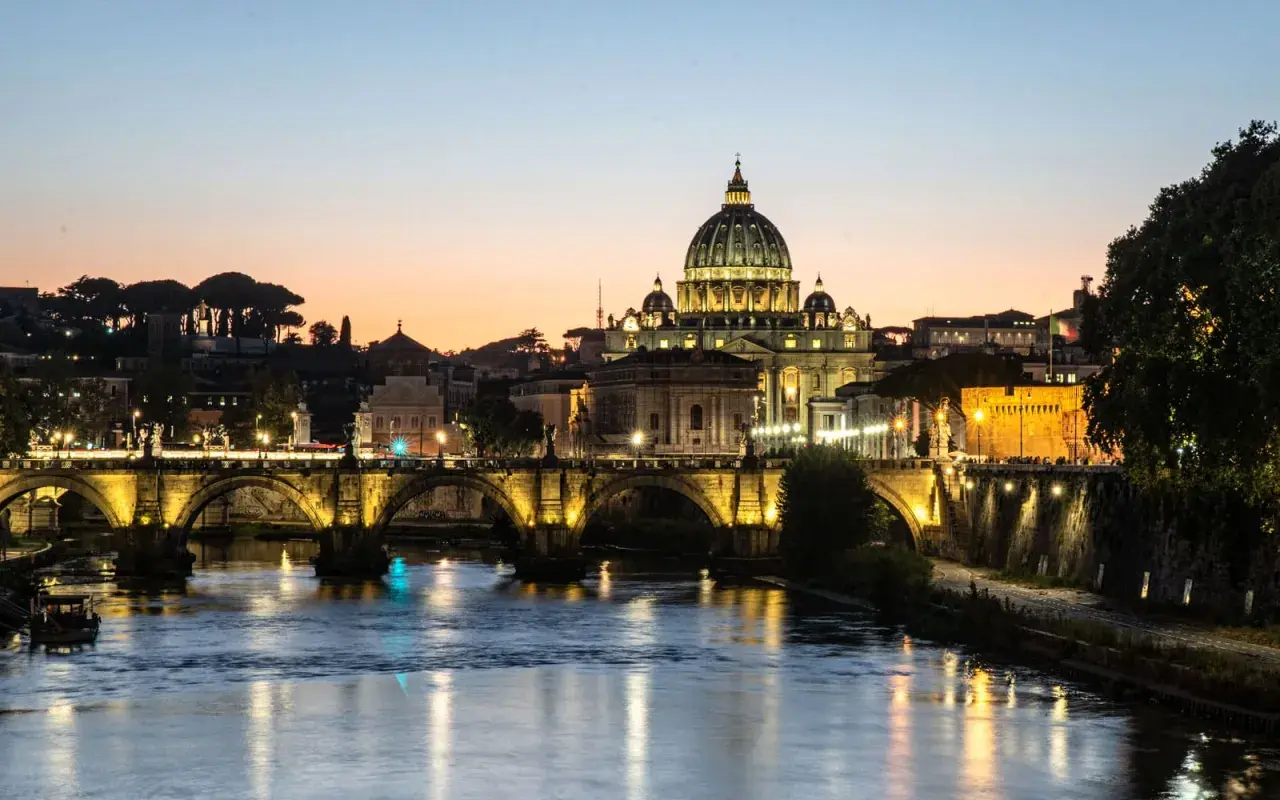 Ponte Sant'Angelo illuminato al tramonto, con Castel Sant'Angelo e la cupola di San Pietro. Un'idea su cosa fare il pomeriggio a Roma.