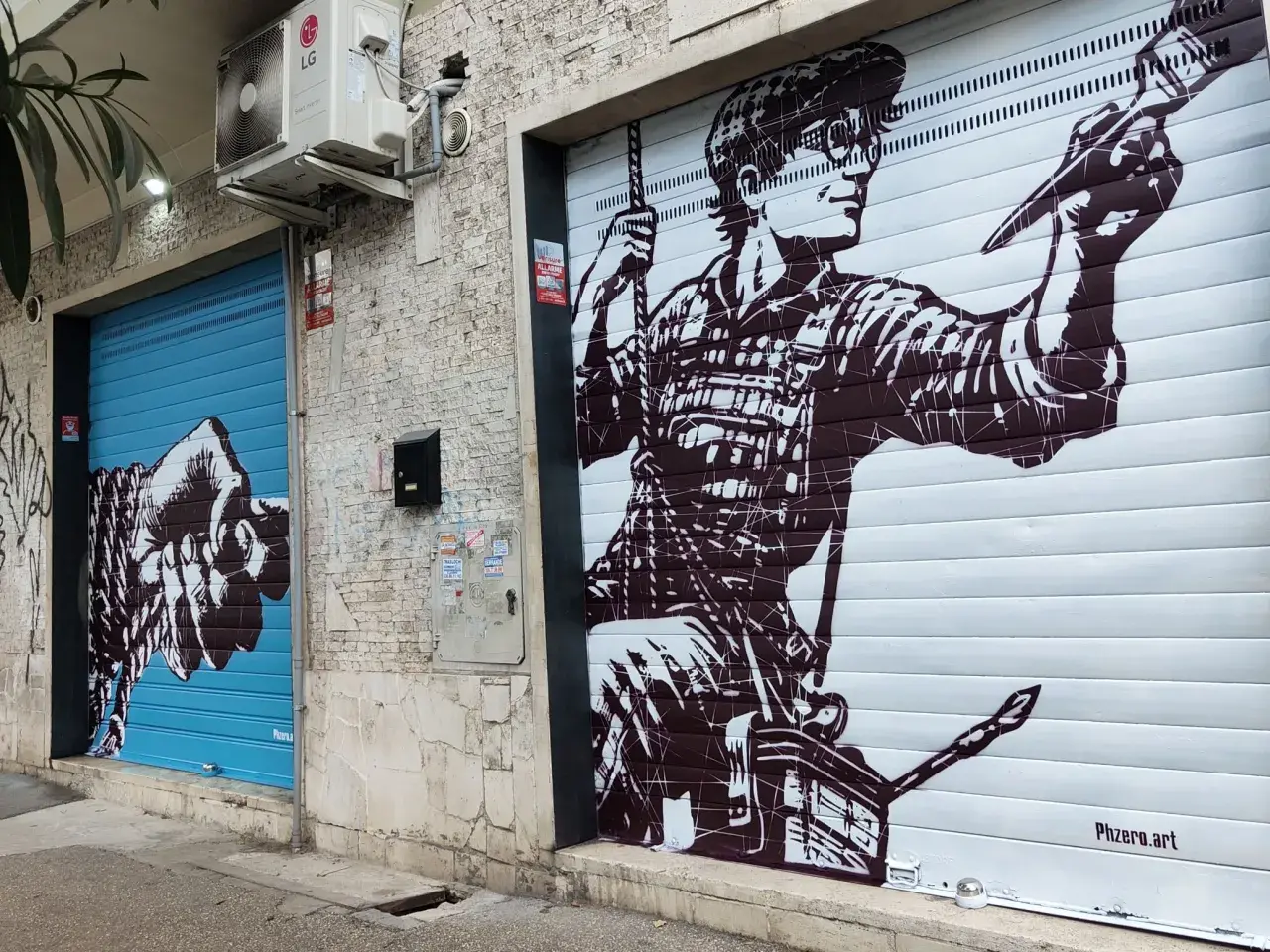 Un pugno su saracinesca blu e un artista al lavoro su un altro saracinesca: arte urbana in un quartiere murales di Roma.