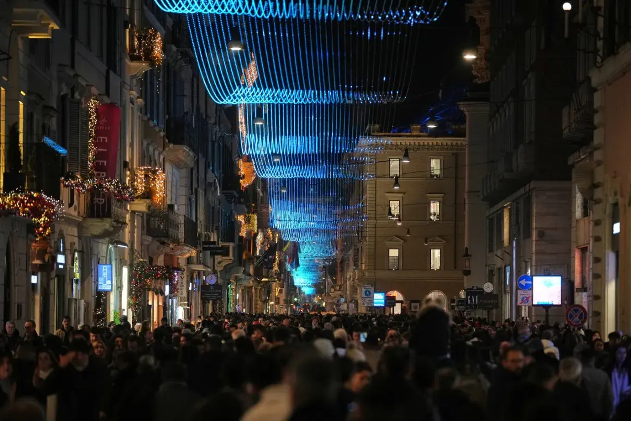 Folla festosa in strada a Roma, 25 dicembre, sotto luminarie blu e decorazioni natalizie.