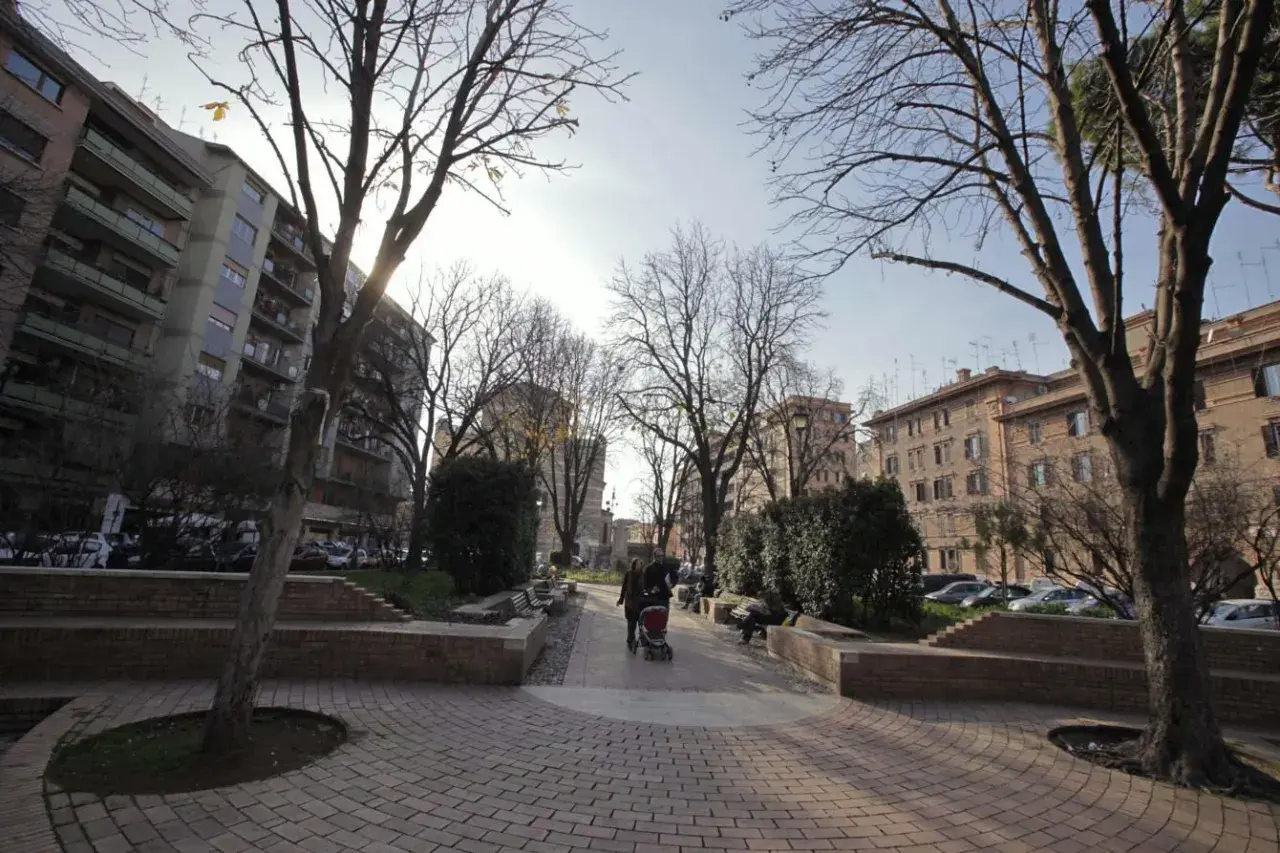 Passeggiata in un parco urbano, ideale per capire come arrivare a Testaccio da Termini. Alberi spogli, palazzi e persone con un passeggino.