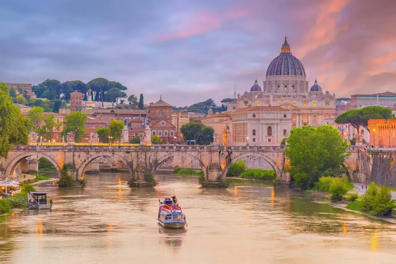 Tramonto su Roma con la maestosa chiesa San Pietro a dominare il paesaggio, mentre un battello naviga sul Tevere.