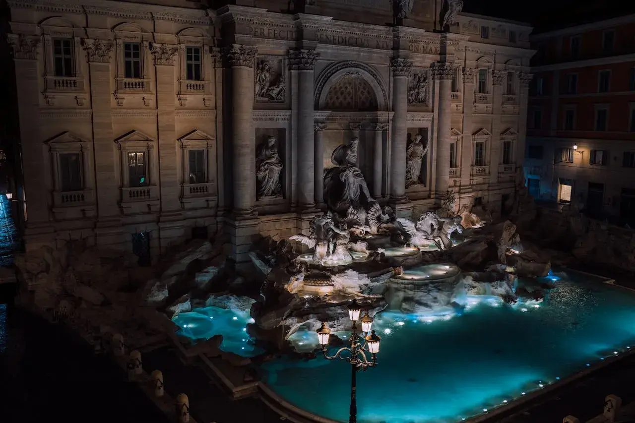 Fontana di Trevi a Roma di notte, con le sue sculture illuminate e l'acqua turchese che brilla sotto i lampioni.