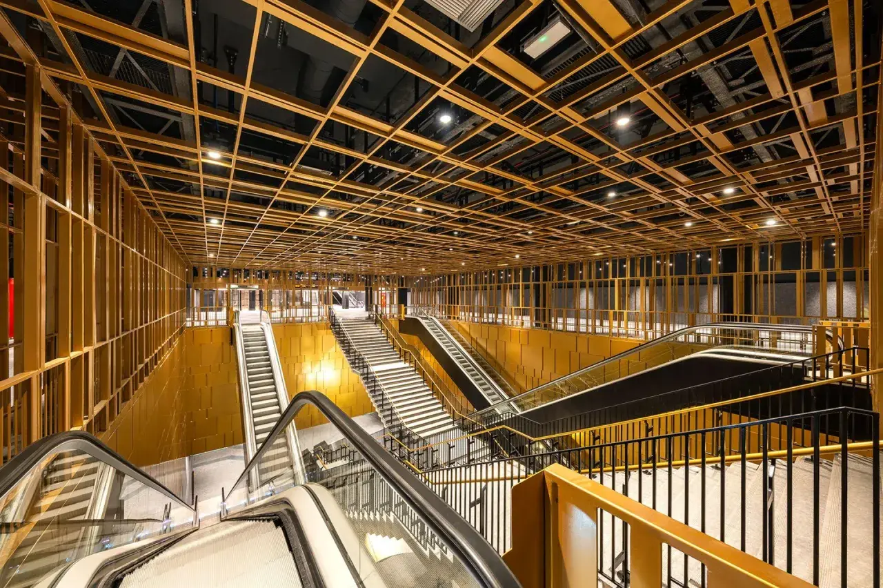 Interni moderni di una stazione metro con soffitto a griglia dorata, scale mobili e gradinate. Un assaggio delle future metro c fermate.