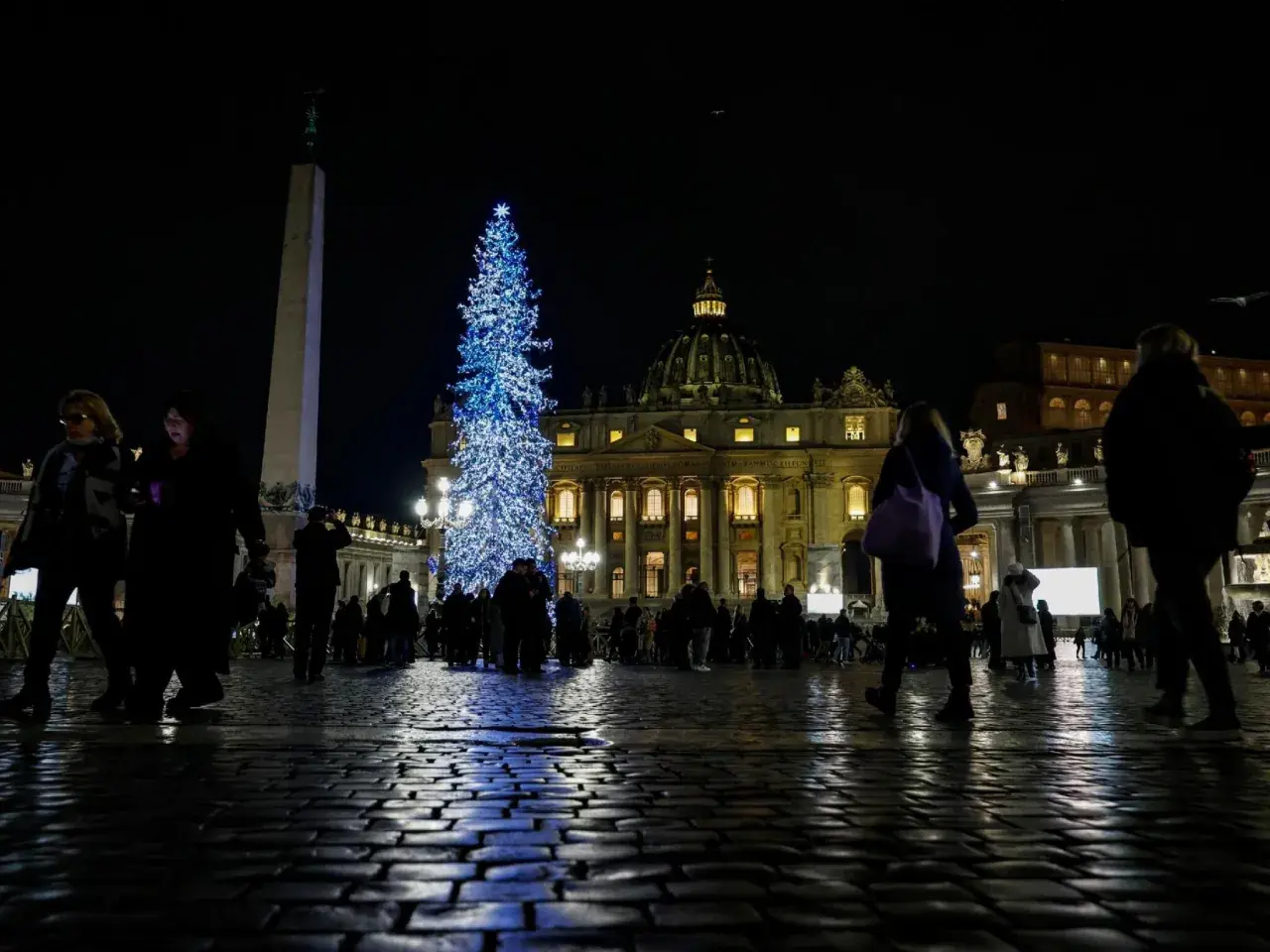 Piazza San Pietro illuminata da un grande albero di Natale blu, con gente che passeggia. Un'idea su cosa fare il 24 dicembre a Roma.
