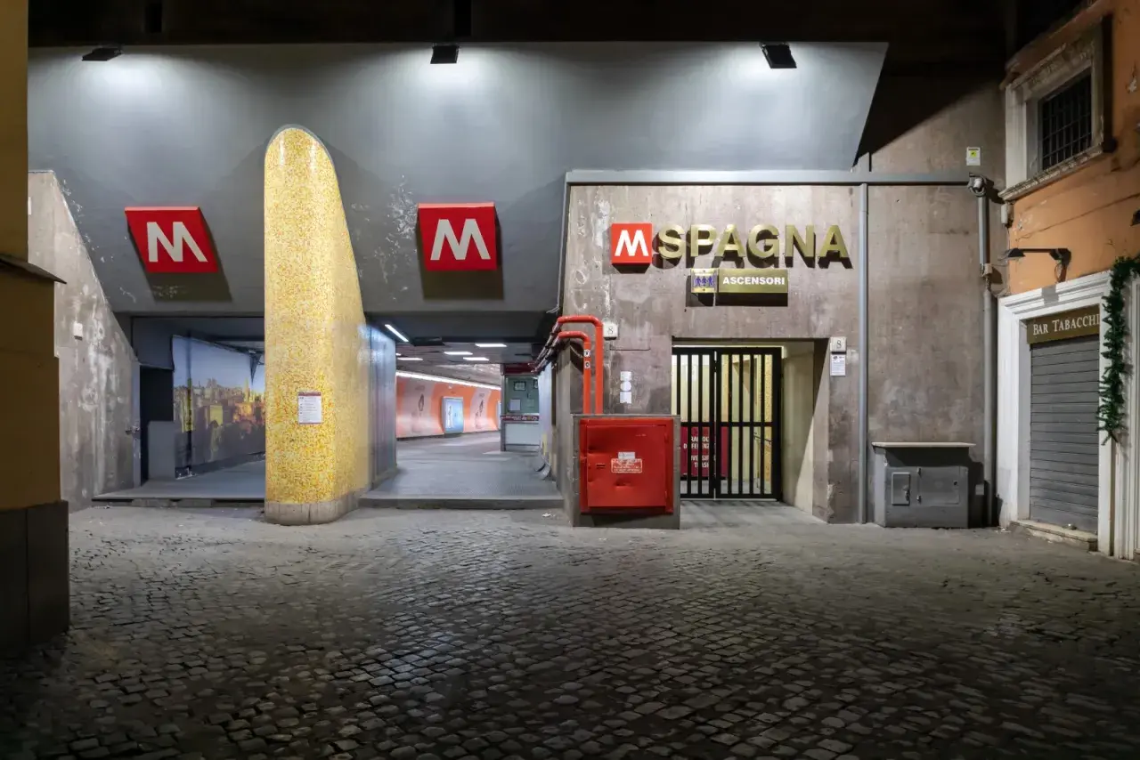 Ingresso della metro a Roma, stazione Spagna, con insegna dorata e pavimentazione in sampietrini.