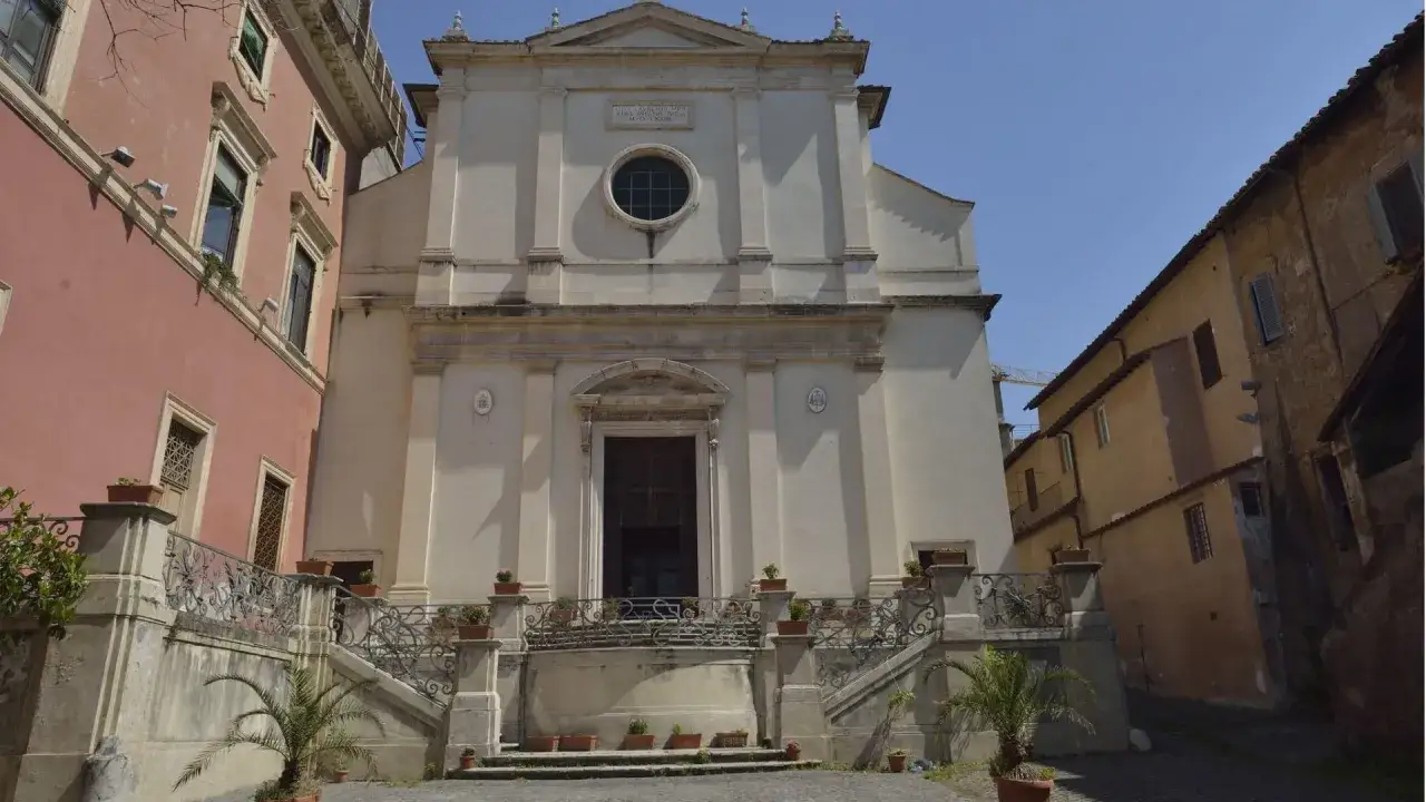 Facciata di una chiesa bianca con scalinata e ringhiera ornata, circondata da edifici colorati. Un esempio di cosa vedere a San Lorenzo, Roma.