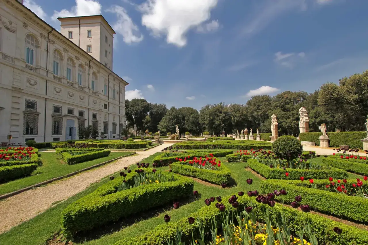 Giardini all'italiana di Villa Borghese a Roma, con tulipani rossi e viola che sbocciano tra siepi curate e statue classiche.