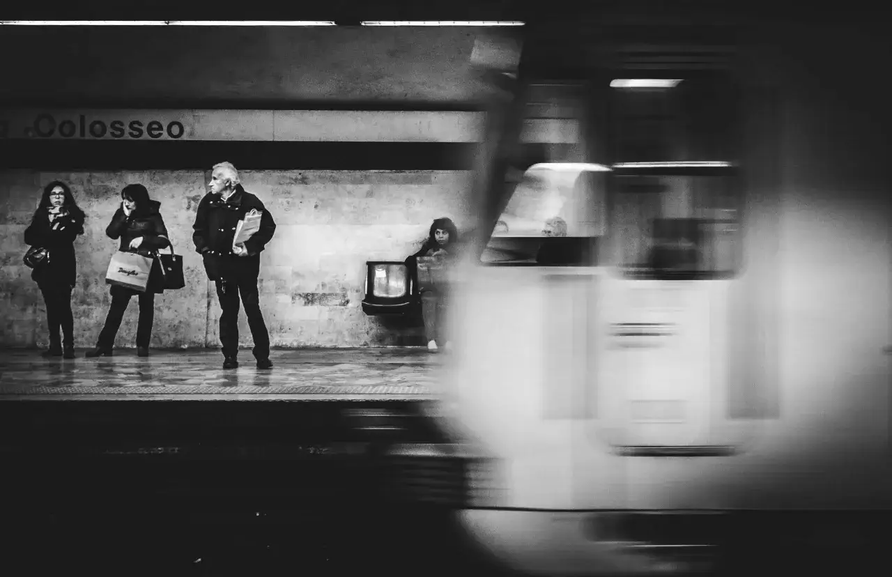 Persone attendono il treno alla stazione metro a Lepanto, mentre un convoglio sfreccia sfocato.