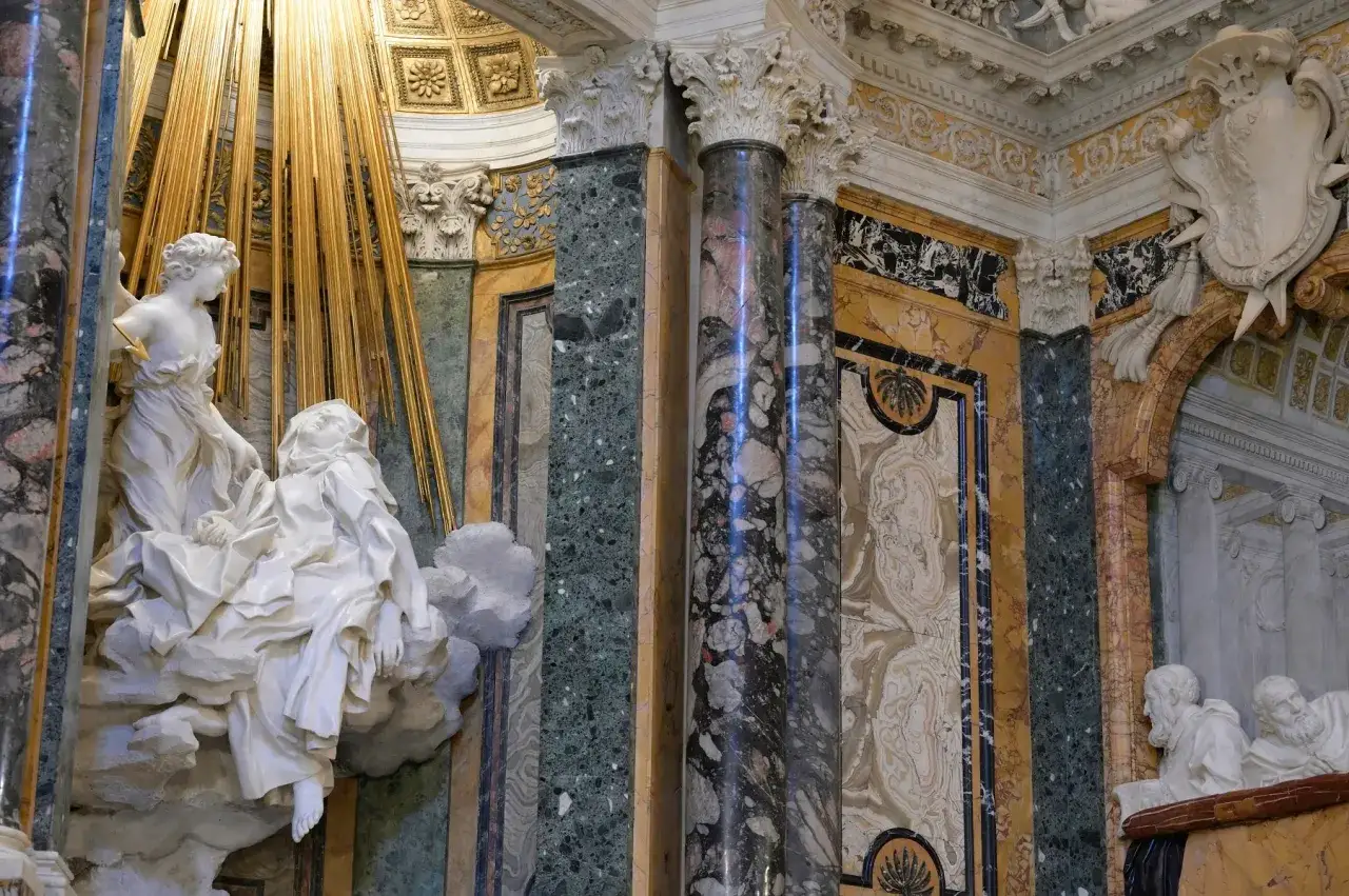 La Cappella Cornaro: un angelo trafigge Santa Teresa con una freccia dorata, circondati da marmi policromi e stucchi barocchi.