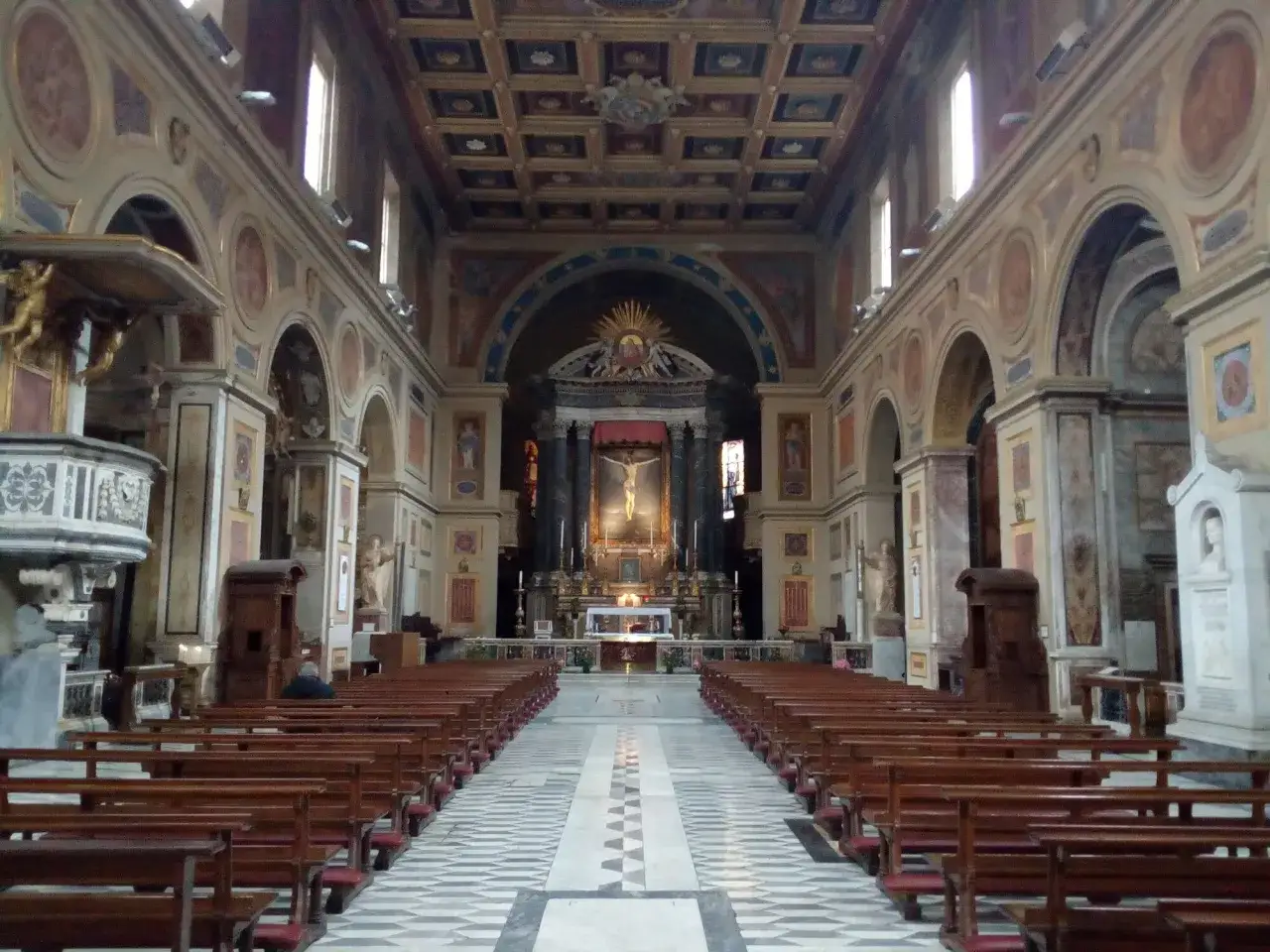 Navata di San Lorenzo in Lucina, con file di panche in legno e un altare imponente.