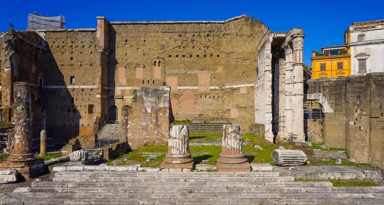 Resti imponenti del Foro di Augusto a Roma, con colonne spezzate e un'antica muraglia che si staglia contro il cielo azzurro.