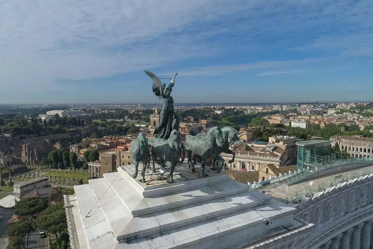 Statua alata su quadriga domina il panorama di Roma, con l'Altare della Patria in primo piano.