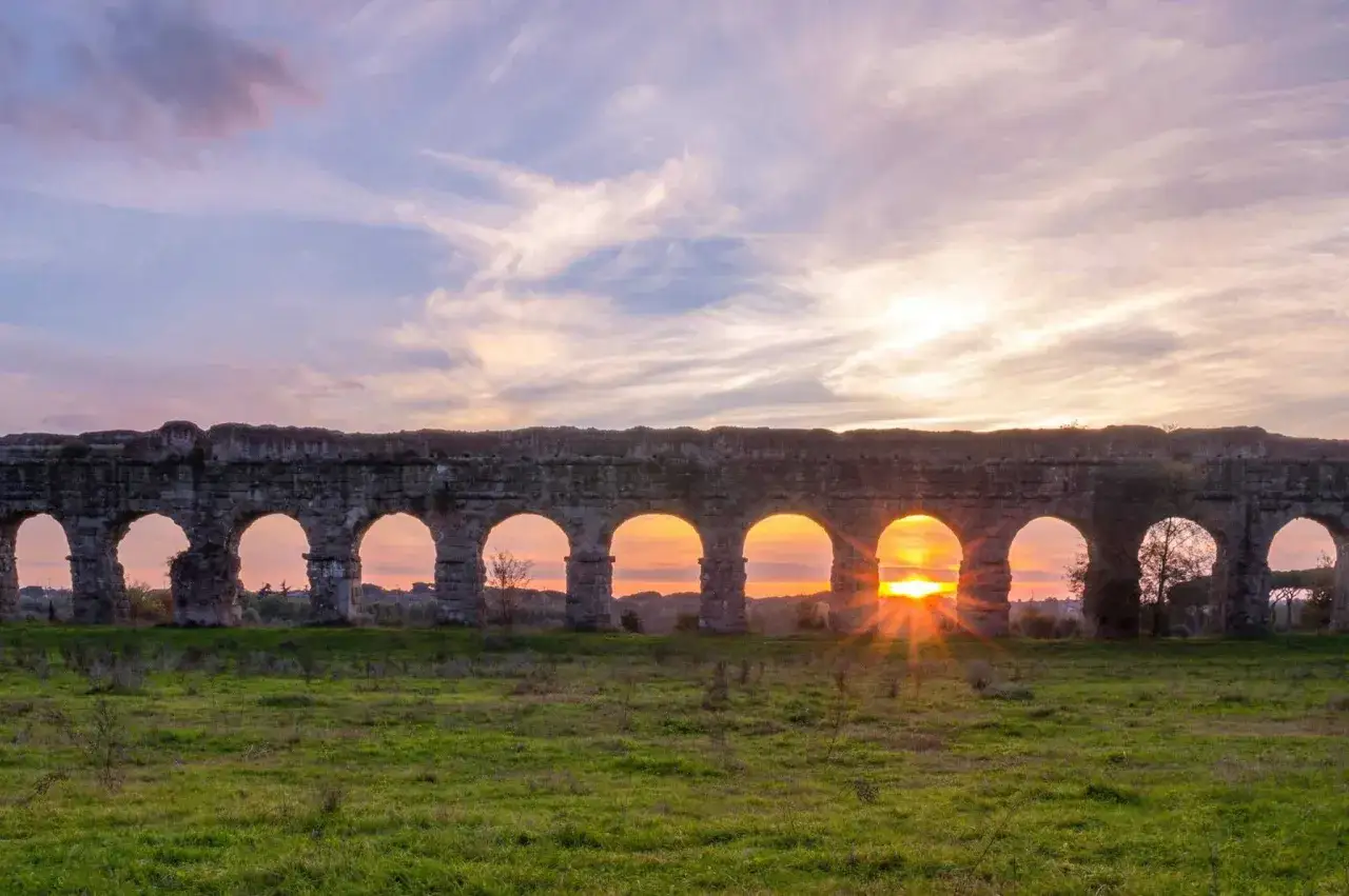 Tramonto dorato attraverso gli archi dell'acquedotto Appio, un antico monumento romano immerso nella campagna.
