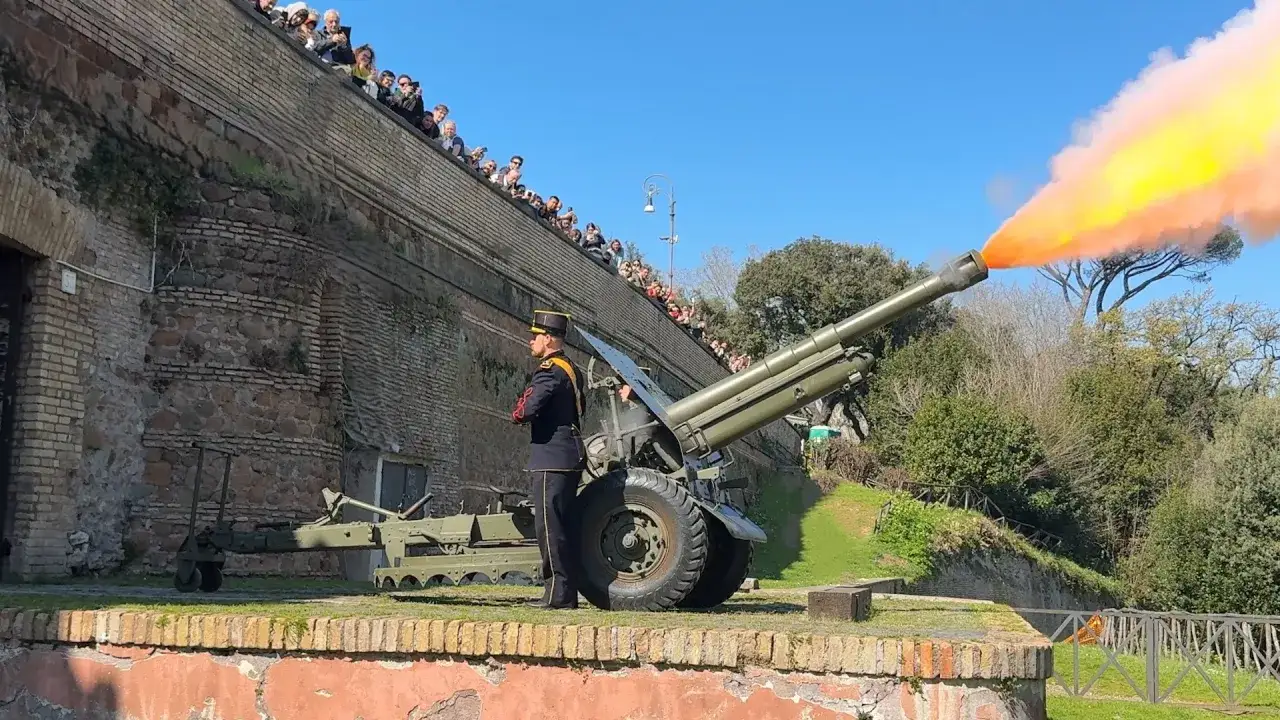 Il cannone del Gianicolo spara fumo colorato, mentre una folla osserva dall'alto.