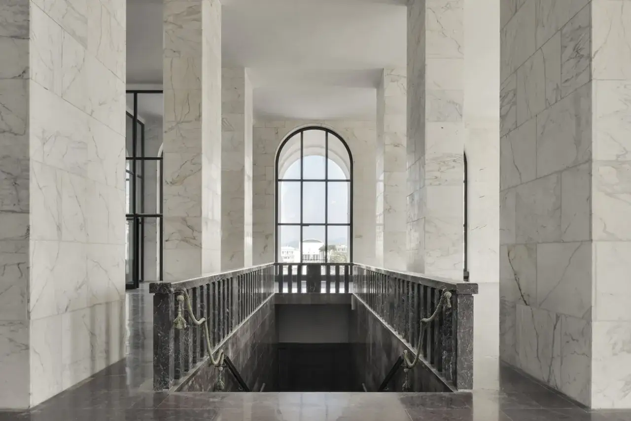 Interno del Palazzo della Civiltà Italiana: un corridoio con colonne in marmo bianco, una scalinata scura e una grande finestra ad arco che si affaccia sull'esterno.