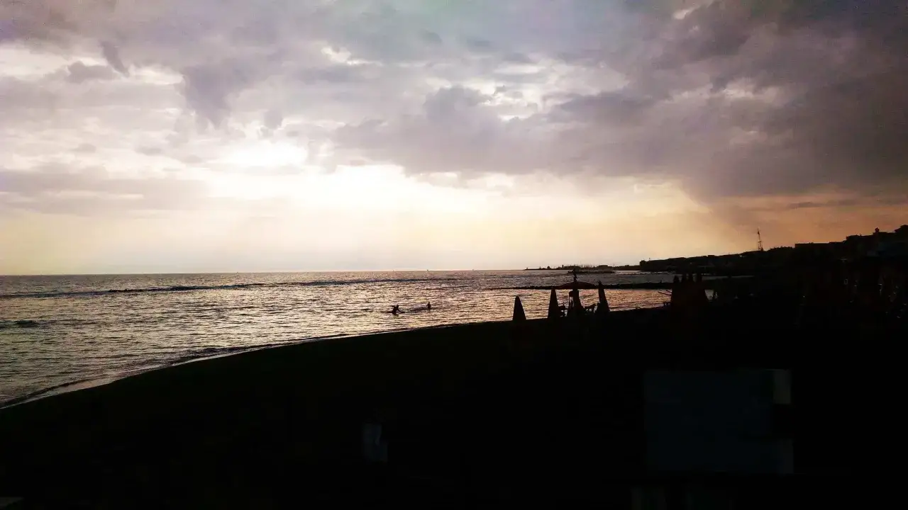 Tramonto a Ostia, con nuvole scure sul mare e la spiaggia con ombrelloni chiusi. Un'idea di cosa vedere a Ostia per una serata tranquilla.