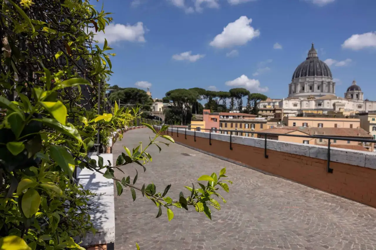 Un percorso lastricato porta verso la cupola di San Pietro, un'ideale passeggiata da Termini a San Pietro a piedi, con la vegetazione in primo piano.