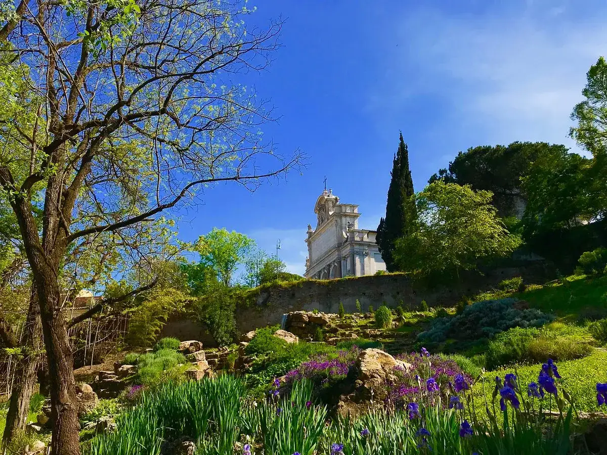 Un angolo fiorito dell'orto botanico di Roma, con iris viola e un edificio storico sullo sfondo.