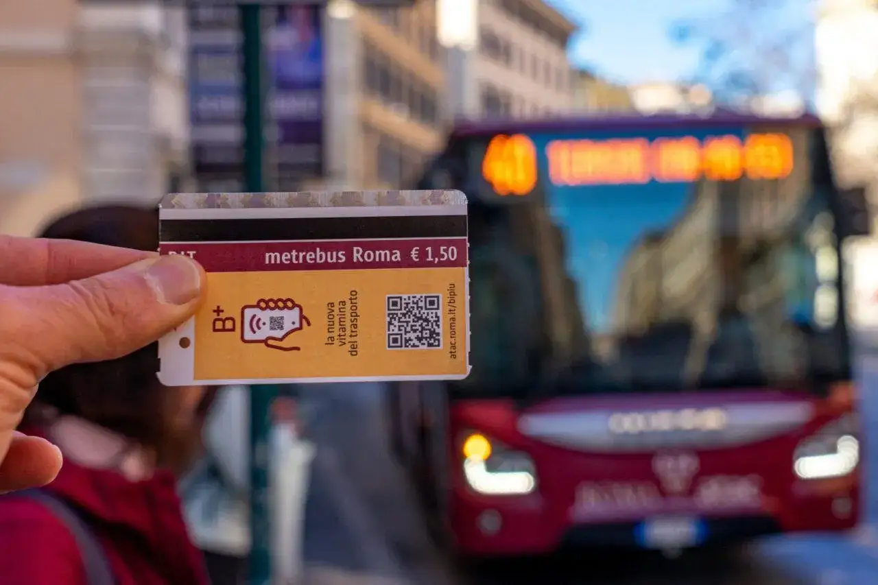 Una mano tiene una tessera metropolitana Roma, con un autobus rosso sfocato sullo sfondo.