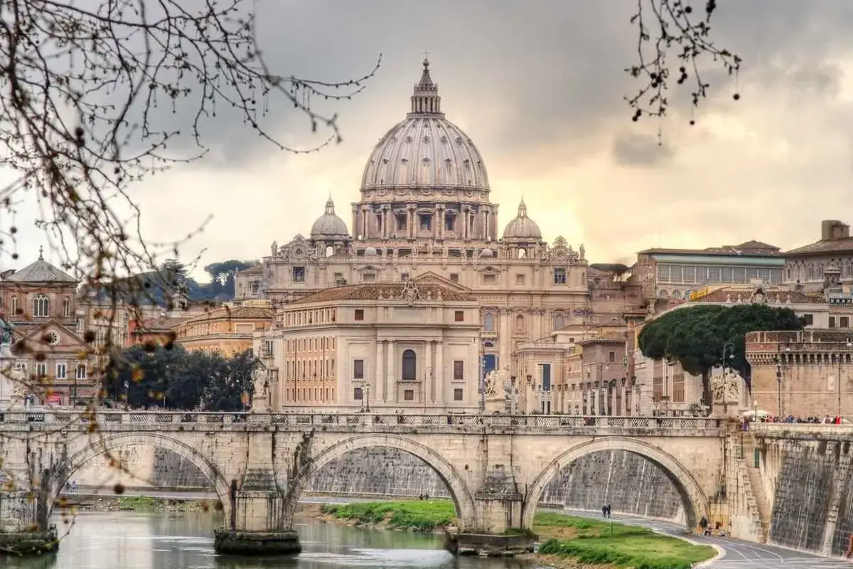 Un ponte di Roma attraversa il Tevere con la cupola di San Pietro sullo sfondo, un'atmosfera suggestiva di inverno a Roma.