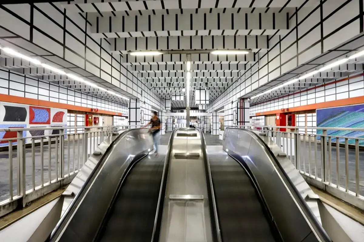 Scale mobili nella moderna stazione metro Vittorio Emanuele a Roma, con pareti e soffitto decorati da un motivo a griglia nera su bianco.