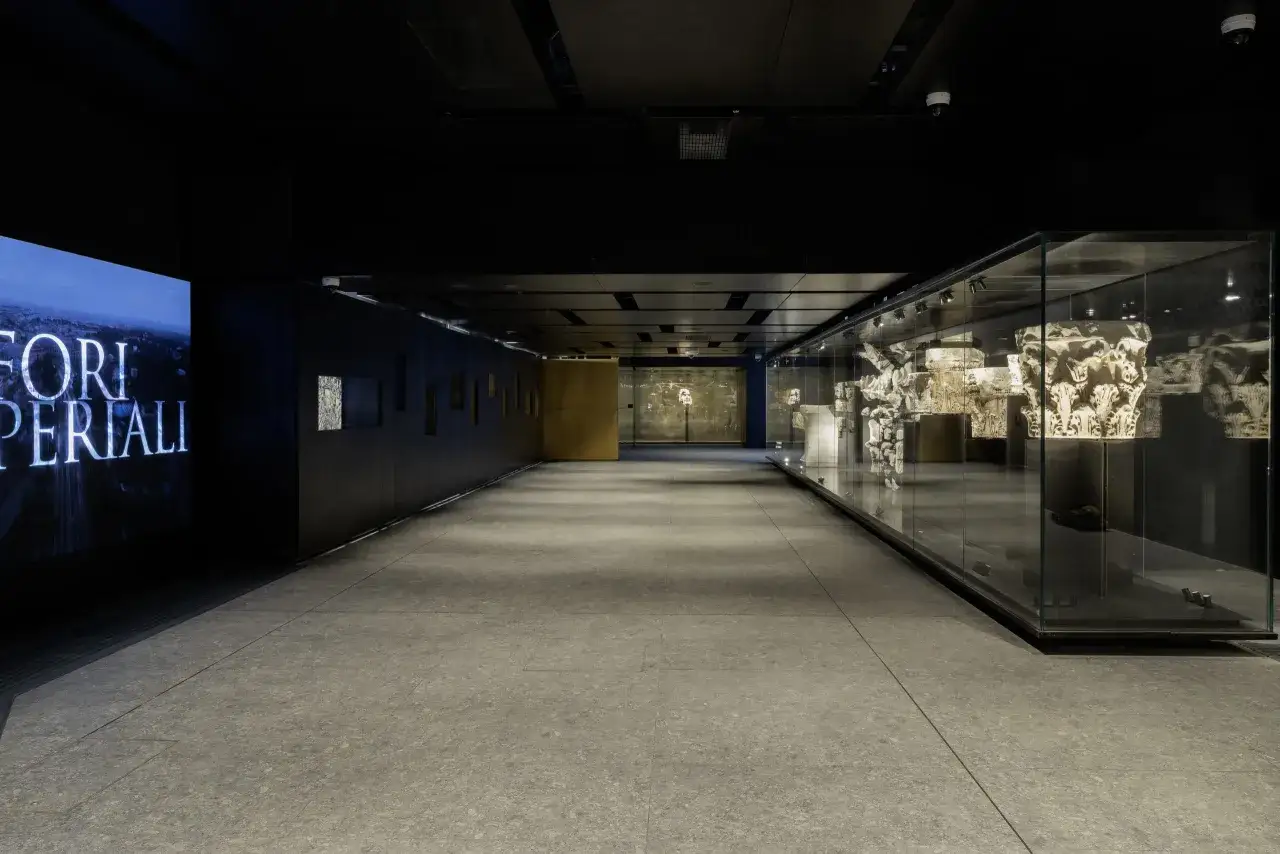 Corridoio moderno con reperti antichi in teche di vetro, un grande schermo luminoso e un'atmosfera che evoca la storia, come quella della metro C Roma Colosseo.