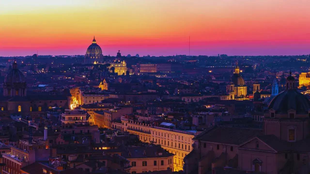 Roma ad agosto, un tramonto infuocato illumina la cupola di San Pietro e i tetti della città eterna.