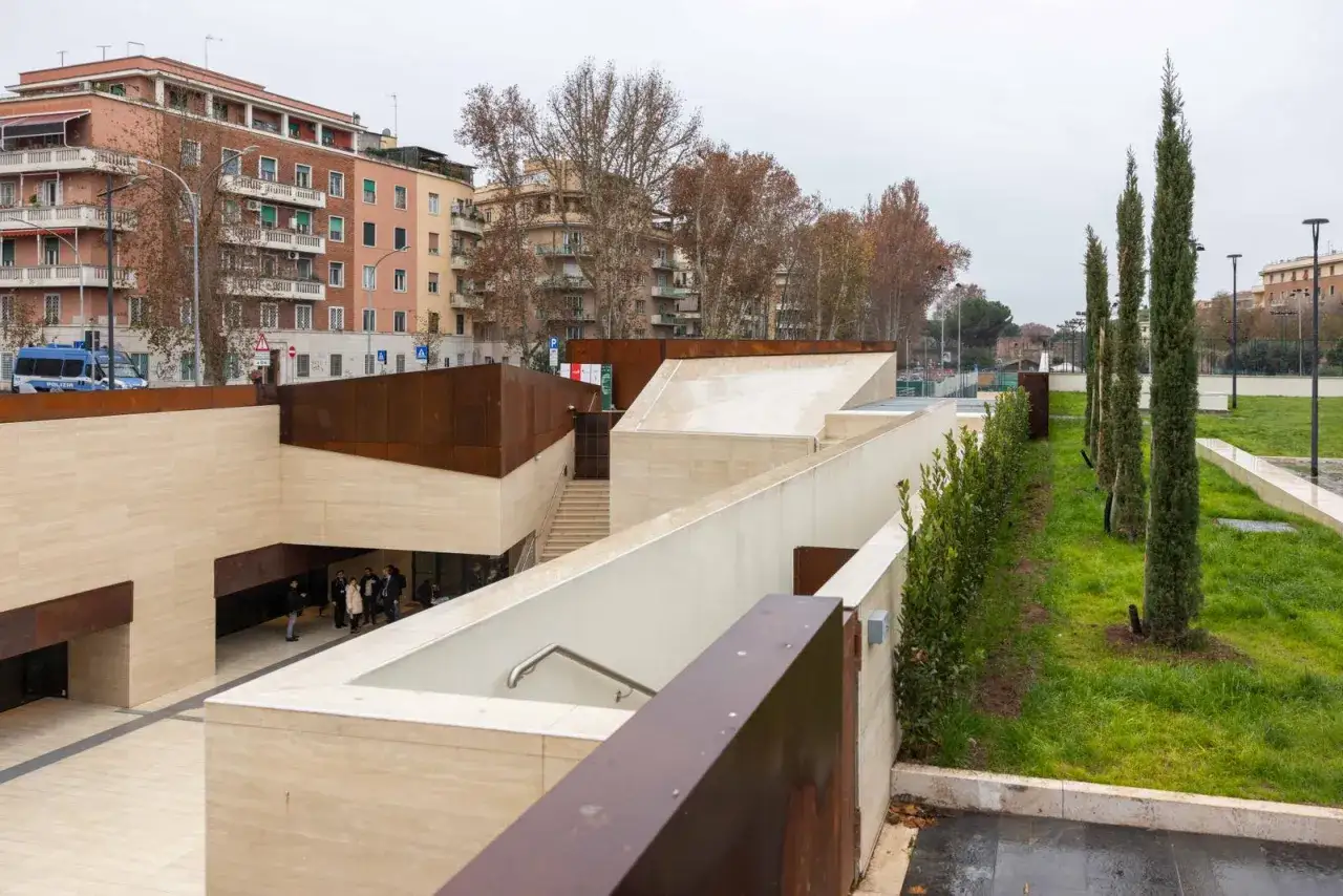 Ingresso moderno alla fermata metro Marconi, con architettura in travertino e corten, circondato da verde e palazzi.