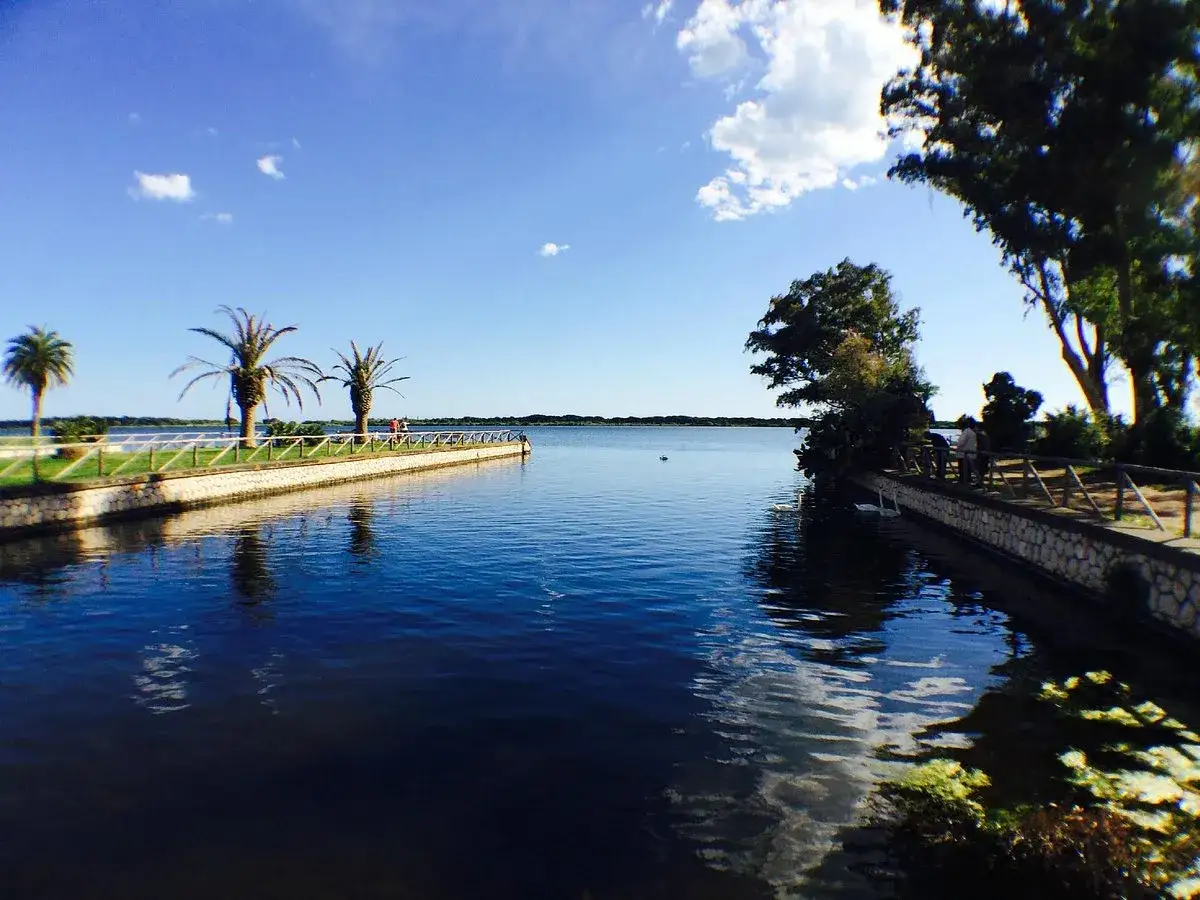 Un lago tranquillo con palme e alberi, un sentiero pedonale e persone che passeggiano: ecco cosa vedere a Latina per un momento di relax.