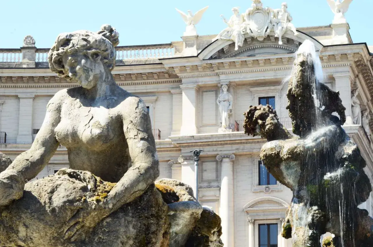 Fontana delle Naiadi a Piazza della Repubblica, Roma. Le statue di pietra e bronzo emergono dall'acqua, con un palazzo bianco sullo sfondo.