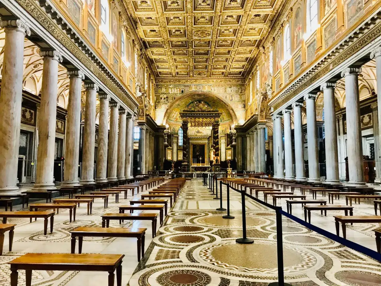 Interno dorato di una delle chiese da vedere a Roma, con file di banchi e colonne imponenti.