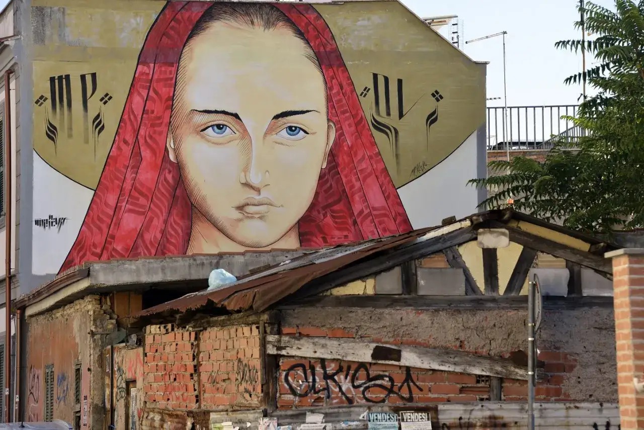 Volto di donna con occhi azzurri e velo rosso, un grande murales pigneto che domina un edificio fatiscente.