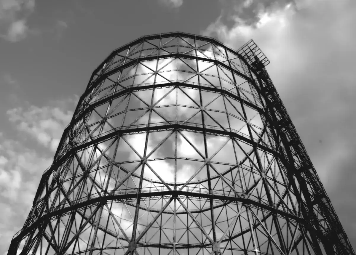 Struttura metallica imponente di un gasometro, con il cielo nuvoloso che si riflette tra le sue travi.