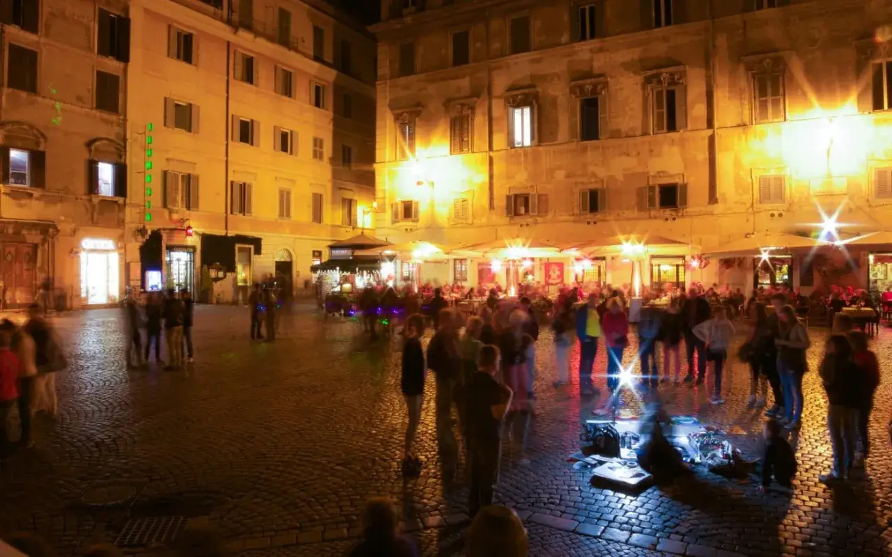 Piazza romana illuminata di notte, gente che passeggia e si gode la serata. Un'idea su cosa fare il sabato sera a Roma.