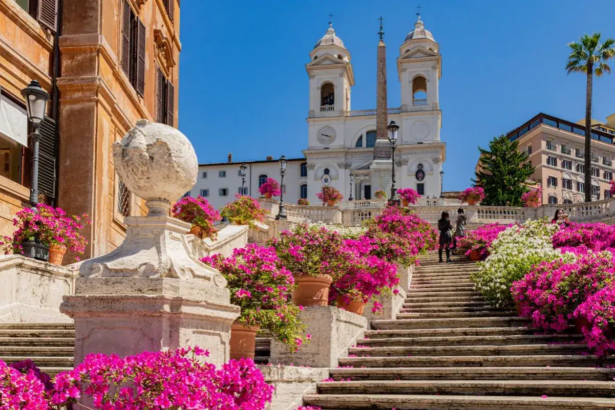 Scalinata di Trinit&agrave; dei Monti a Roma, fiorita di rosa e bianca, con la chiesa sullo sfondo.