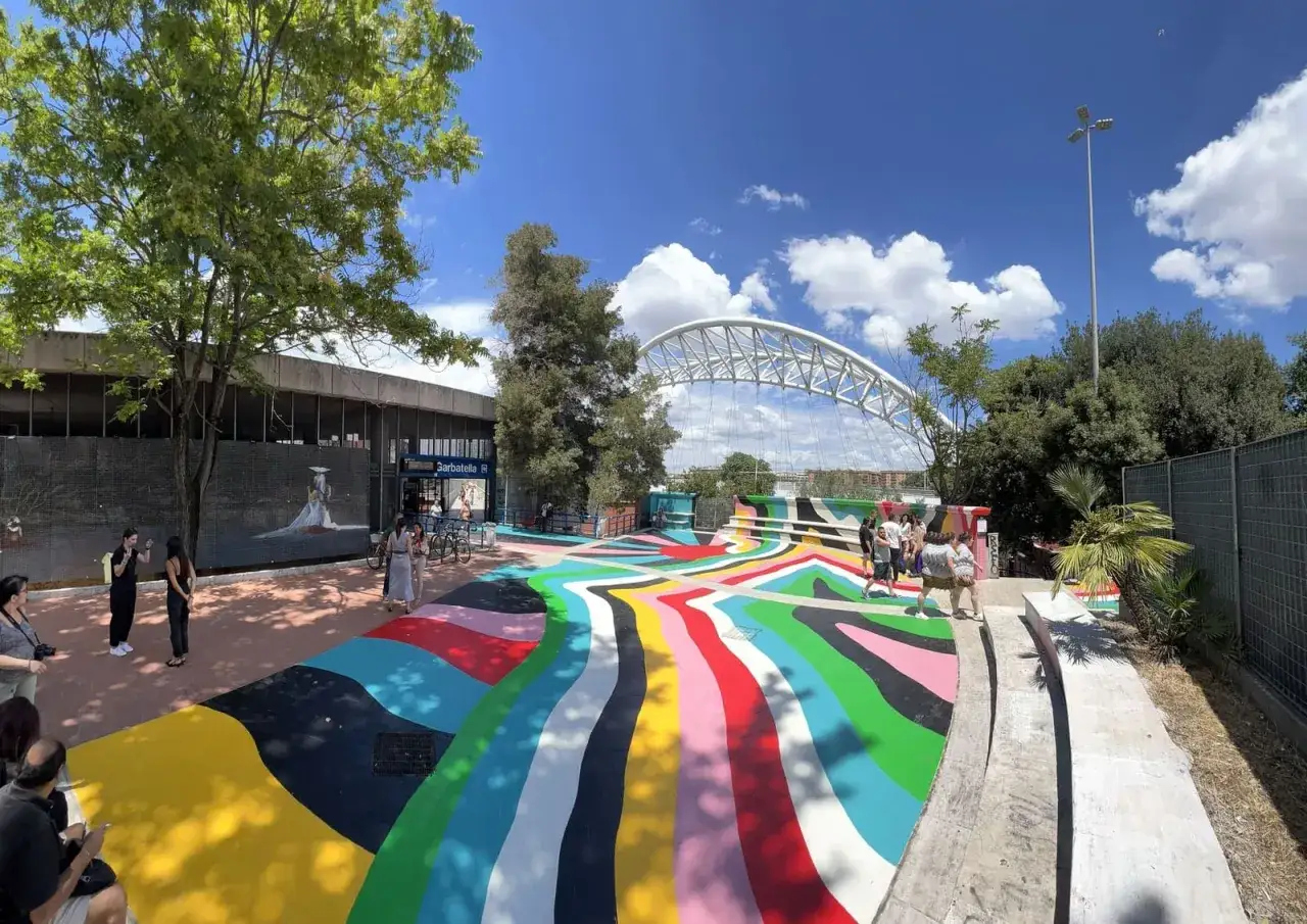 Area colorata e vivace vicino alla metro Garbatella Roma, con persone che passeggiano e un ponte moderno sullo sfondo.