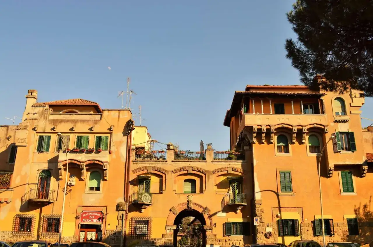 Edifici color ocra a Garbatella, cosa vedere: un arco centrale, balconi in ferro battuto e finestre verdi sotto un cielo azzurro.